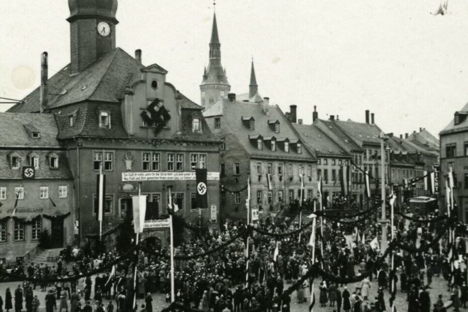 Blick auf den Marktplatz mit dem Rathaus in Waldenburg/Sachsen von der heutigen Altenburger Straße aus, die im Rahmen der Olympischen Sommerspiele 1936 festlich geschmückt sind.