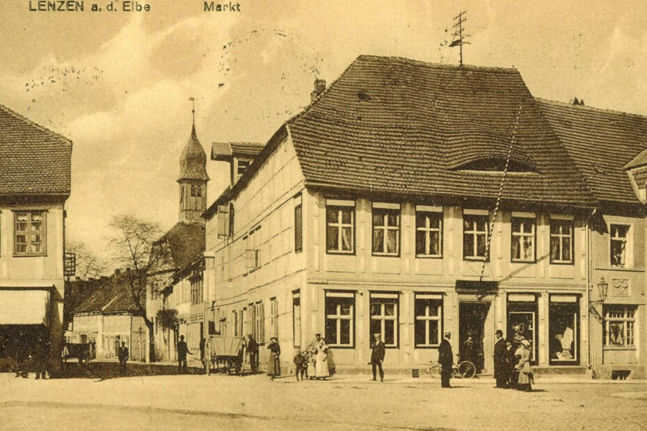 Postkarte aus Lenzen aus 1926, das den Markt zeigt. Im Mittelpunkt ein großes Gebäude, rechts und links davon gehen Straßen ab.