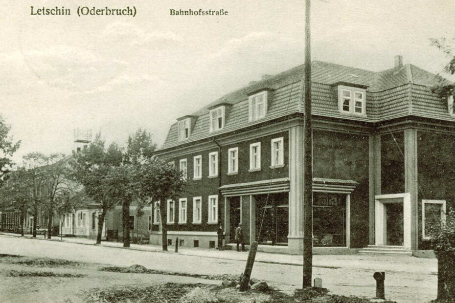 Bahnhofstraße Letschin 1928. Im Mittelpunkt steht eine Straße und ein großes Gebäude, vorne im Bild steht ein großer Strommast.