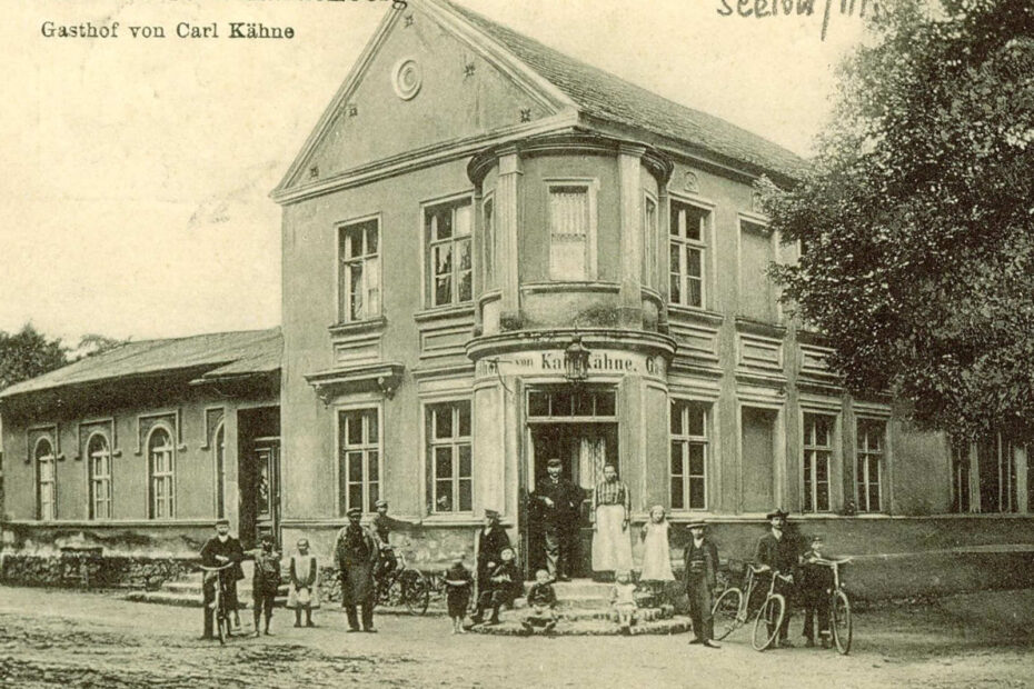 Postkarte aus Neu-Hardenberg, das den Gasthof von Carl Kähne zeigt. Vor dem Gasthof halten sich mehrere Menschen auf.