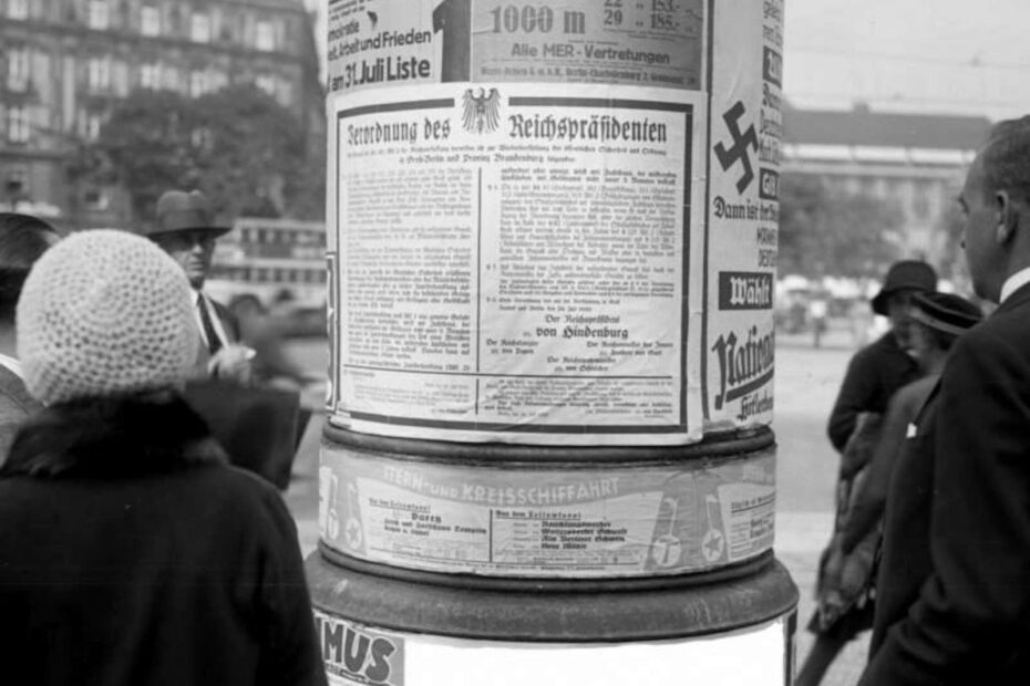 Ein Bild von der Verordnung des Reichspräsidenten von Hindeburg über den Ausnahmezustand einer einer Litfassäule in den Straßen Berlins. Rechts und links im Bild sind mehrere Menschen.