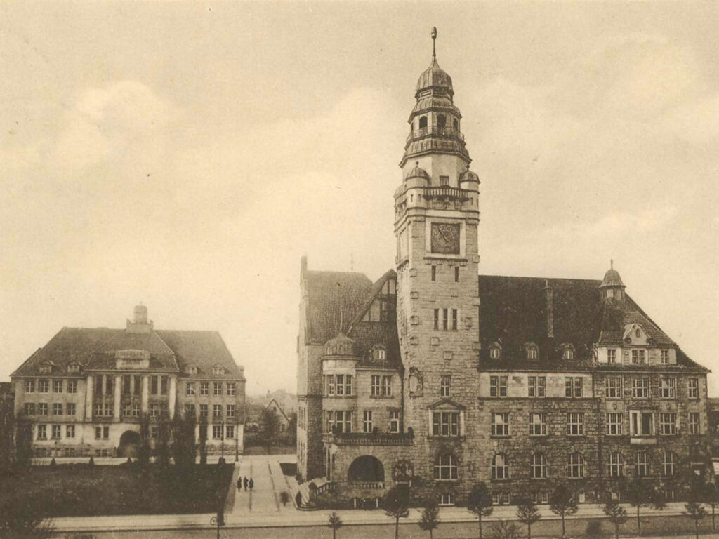 Bild aus 1929, auf dem das Rathaus mit Lyzeum abgebildet sind. Rechts großes Gebäude mit Turm in der Mitte, links steht ein kleineres Gebäude, dessen Front aus vier Säulen besteht.